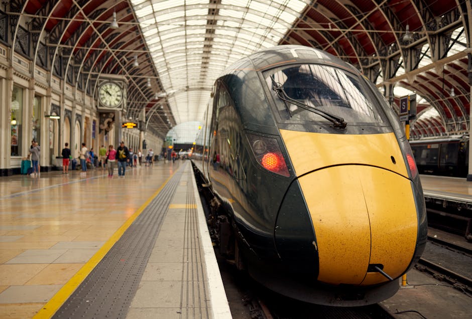 Inside a spacious train station with a high, curved glass and metal roof, an empty platform is visible along with a parked train on the right side. The station includes decorative architectural detail